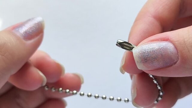Female hands fastening a ball chain with a small connector, close up of a metal ball chain and clasp, jewelry accessory, tag attachment and small fastening hardware concept.