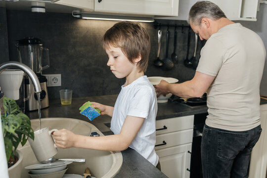 Boy and father doing dishes together in kitchen