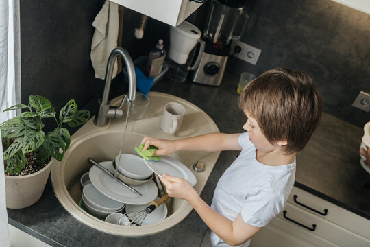 Child washing dishes in kitchen sink learning responsibility