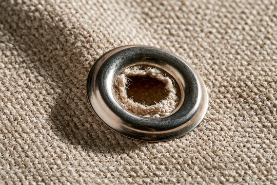 Metal eyelet on beige woven fabric close up  