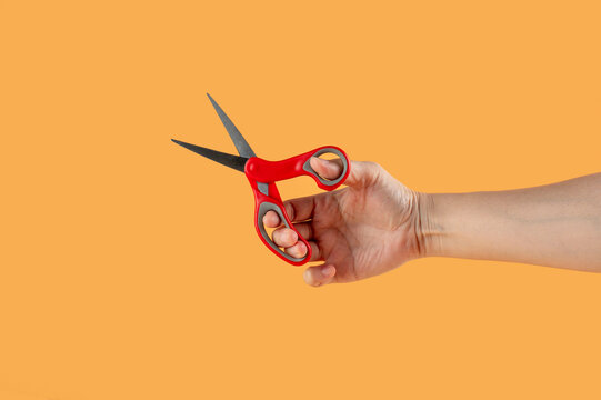 Hand holding office stationery scissors cutting on cream background.