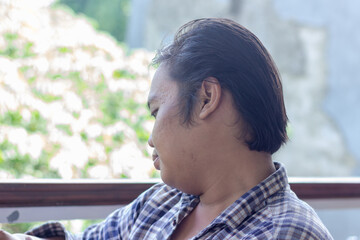Candid side profile portrait of a young Asian man looking down outdoors. © BANG PELOG