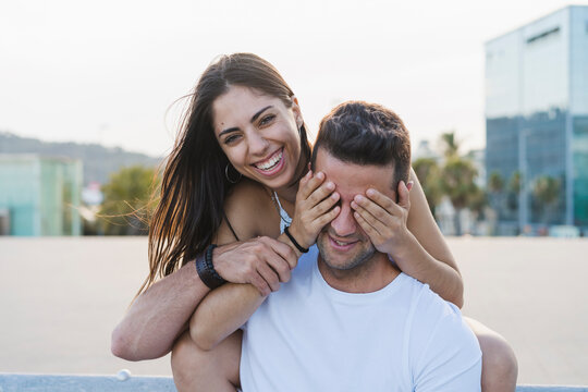 Laughing young woman surprising her boyfriend, covering his eyes
