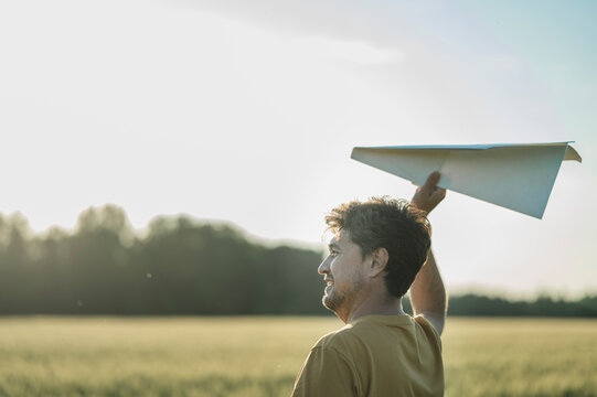 A smiling man launches a paper airplane in a summer field