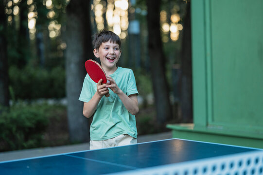 A smiling boy plays table tennis outside in the park