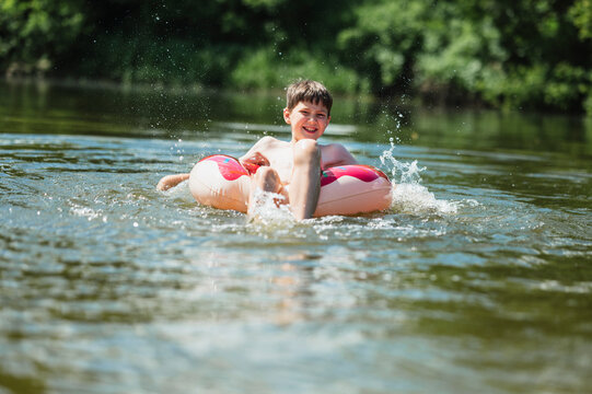 Boy splashes water while swimming in a river with a swimming ring