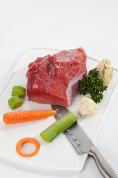 Raw piece of beef with vegetables on chopping board, close up