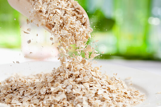 Oat flakes pouring from wooden scoop, close up