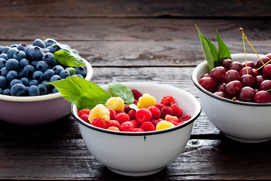 Three bowls sour cherries, raspberries and blueberries on dark wood
