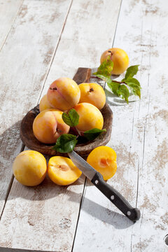 Sliced and whole yellow gages (Prunus domestica subsp. italica) and a wooden spoon on white wooden table, studio shot