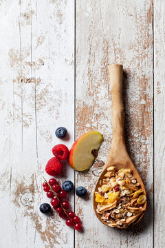 Wooden spoon of granola with dried fruits and various fresh fruits on wood
