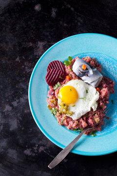 Plate of Labskaus with potatoes, rollmops, pickled gherkin, beetroot and fried egg