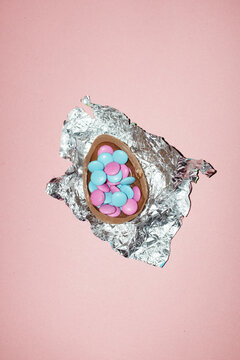 Chocolate Easter egg filled with colorful candy on pink background