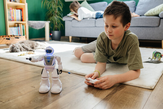 A boy plays with a remote control toy robot on the living room floor