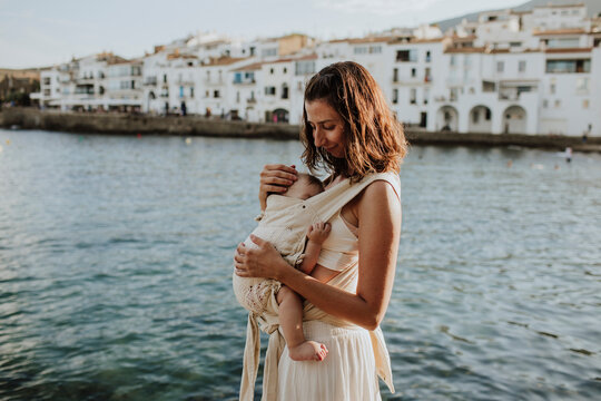 Mother carries her baby in a carrier near the sea in Spain