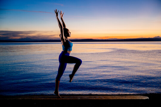 Hispanic woman performing an acrobatic yoga pose on a shore