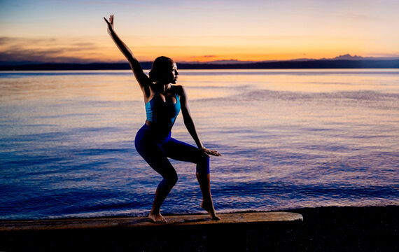 Hispanic woman balancing on wooden bench by ocean at sunset in the USA