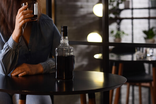 Alcoholism and addiction, woman drinking whiskey alone at a bar table with a bottle of liquor mental health struggles and substance abuse