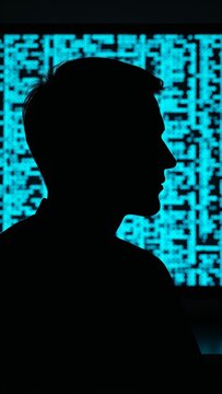Anonymous person silhouette in profile against a bright screen with abstract glowing blue data, symbolizing cyber security and hacking