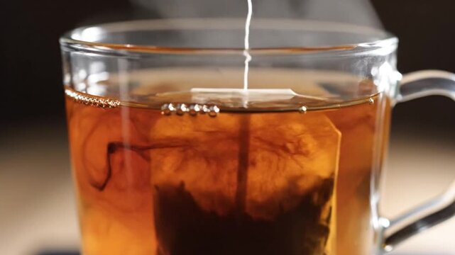 Tea bag infusing in hot water in a clear glass cup, releasing color and aroma