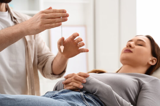 Male psychologist with pendulum hypnotizing woman on couch in office, closeup