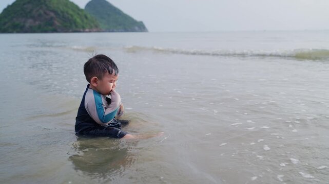 Toddler enjoying water play at beach shore during warm sunset family vacation.