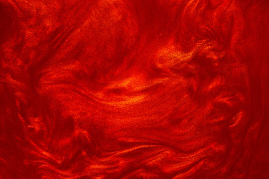 Shimmering red abstract background. Liquid glitter paint texture waves and swirls. Beautiful shiny red glitter texture. Metallic paint close-up as a holiday background.