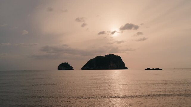 Wide shot of golden sunset over tropical ocean with limestone islands silhouette.