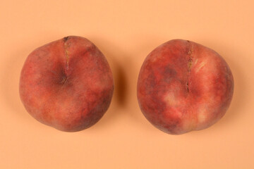 A top view of two whole ripe flat saturn peaches placed next to each other on a matching solid peach colored surface. © nahhan