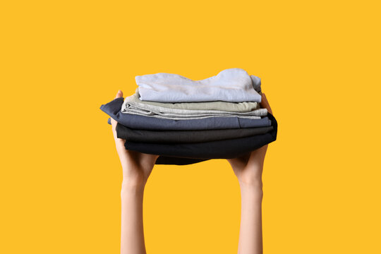 Female hands with stack of different clothes on yellow background