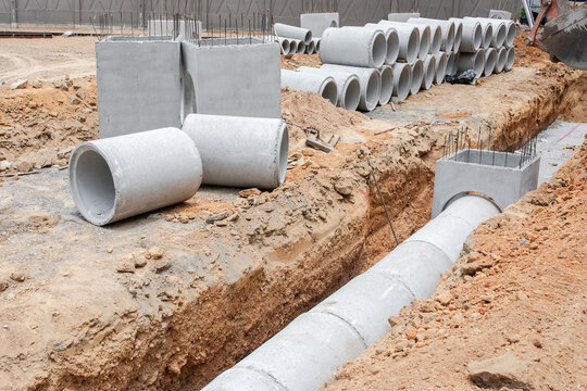 Concrete drainage pipe and square culvert section sit installed inside dug trench, structure allows road runoff to drain into buried system, storm water setup nears construction completion