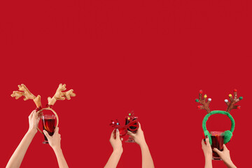 Female hands with glasses of warm mulled wine and Christmas reindeer horns on red background © Pixel-Shot