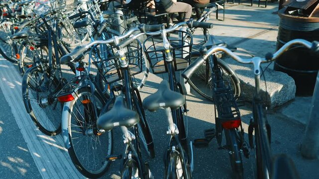 Close-up camera move across a row of parked bicycles on a Copenhagen street, Denmark, showing handlebars, saddles and wheels in a dense bike parking area on a sunny day