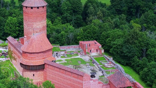 Drone view over the red brick walls and main tower of Turaida Castle, highlighting the medieval fortress architecture surrounded by woodland in Gauja National Park, Latvia aerial close up