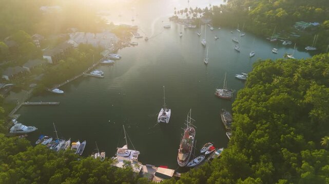 Drone parallax shot captures Marigot Bay bathed in warm golden light with anchored yachts scattered across calm water surrounded by mangroves