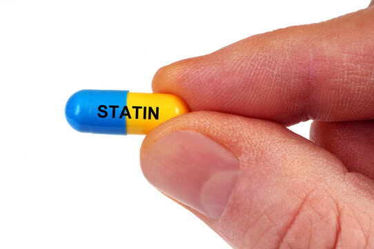 Concept de g&eacute;lule de statine tenue en main en gros plan isol&eacute;e sur fond blanc