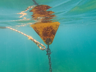 Weathered yellow mooring buoy anchored with a metal chain and rope floating in the crystal clear turquoise waters of the Mediterranean Sea. © Dmitri