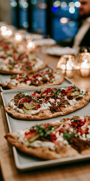 A row of delicious flatbread pizzas topped with white sauce, red peppers, and herbs, ready to be served at an event