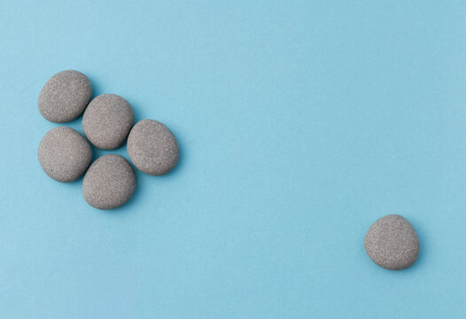 Gray pebbles arranged in cluster with one separate on blue background representing isolation or individuality concept