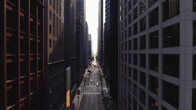 Cinematic drone flight through a downtown Chicago street corridor framed by towering office buildings, traffic, and dramatic urban architecture.