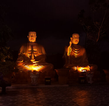 Two serene sitting Buddha statues at Chua Da Bao Pagoda in Nha Trang, Vietnam. Peaceful spiritual scene in a traditional temple at night time