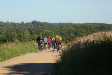 A group of cyclists riding along a rural dirt road, captured from behind, showcasing an active outdoor adventure. Ideal for themes of travel, fitness, friendship, and exploring the countryside togethe © sociopat_empat