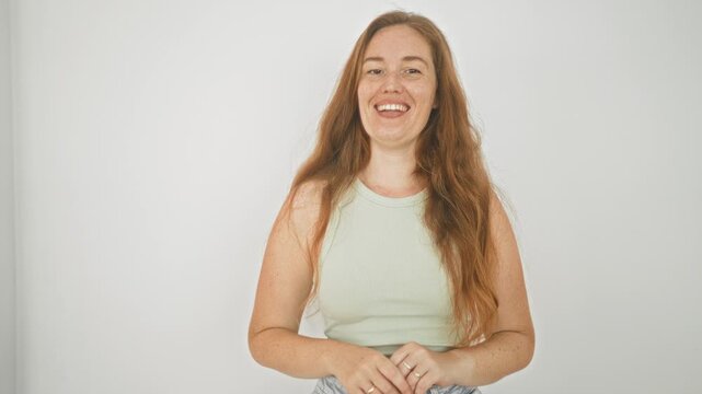 Woman makes ok sign with right hand, smiling and looking at camera in a studio, wearing a light green tank top and rings on her fingers; confidence approval.