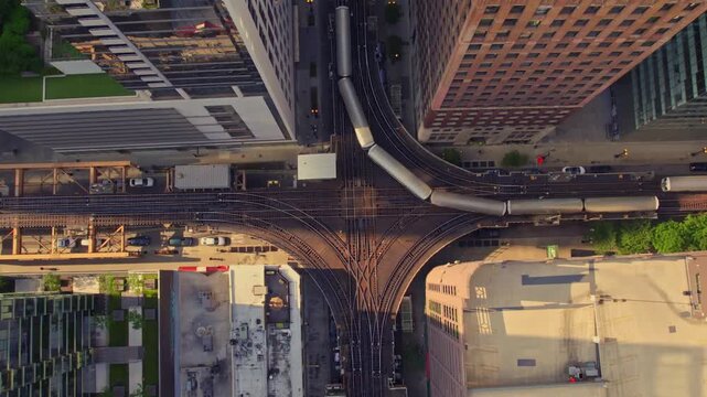 Top-down drone view of multiple CTA trains navigating curved elevated tracks through downtown Chicago between high-rise buildings and city streets.