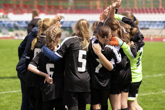 Youth Girls Soccer Team in Black Jerseys Gathering in Pre-Match Huddle Raising Hands - Football Team Unity, Motivation, and Leadership on Field