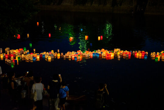 Scenic night landscape view of glowing lanterns floating on a dark river during a traditional festival in Japan