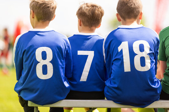 Junior Soccer Substitutes in Blue Shirts Numbers 8, 7, and 18 Sitting on Sideline Bench - Youth Football Team Support During Match