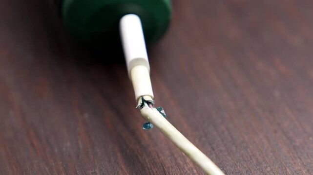 Damaged frayed power cord of an electric tool on a wooden surface. Broken white charger cable insulation with exposed wires. Electricity hazard concept