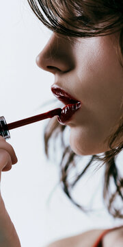 A woman applying deep red lipstick with a glossy finish, her lips slightly parted in concentration