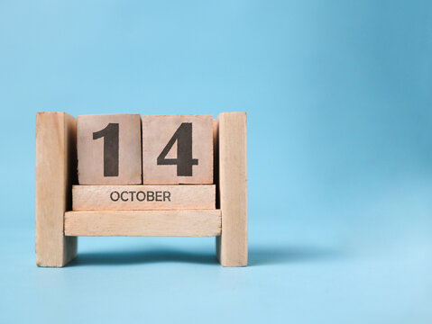 A wooden block calendar for October 14th on a light blue background